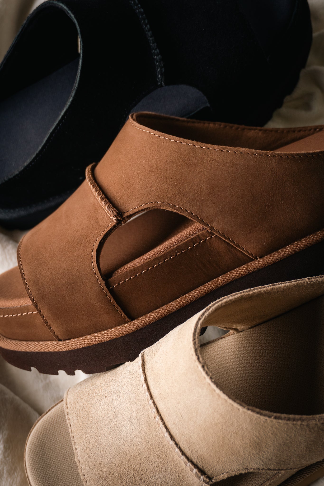Close-up of black, brown, and beige comfort sandals with soft suede-style uppers and cushioned soles.